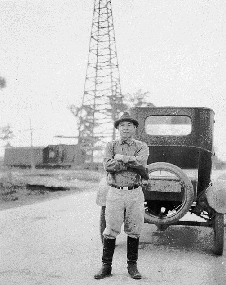 Photo of man in front of car and oil derrick at Orangefield, Texas