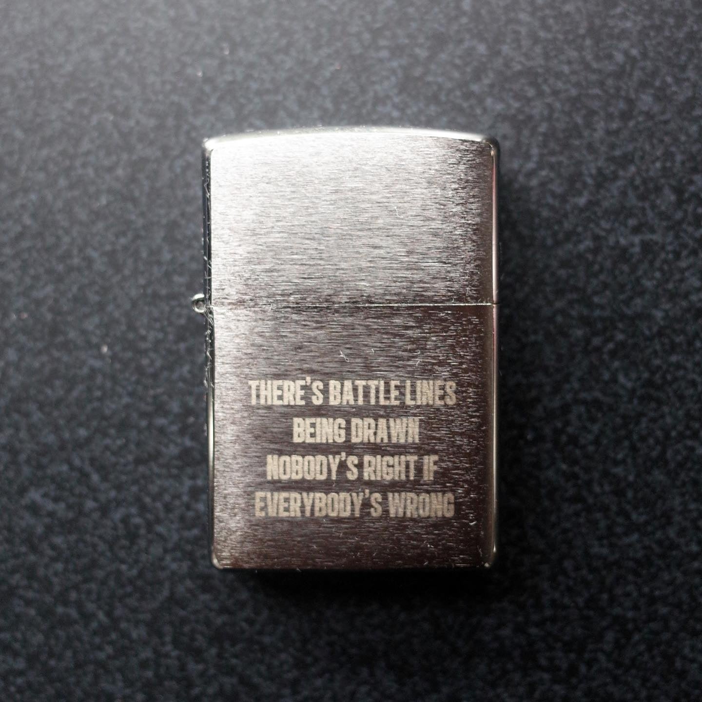 A Zippo style lighter with the engraving, "THERE'S BATTLE LINES BEING DRAWN NOBODY'S RIGHT IF EVERYBODY'S WRONG"