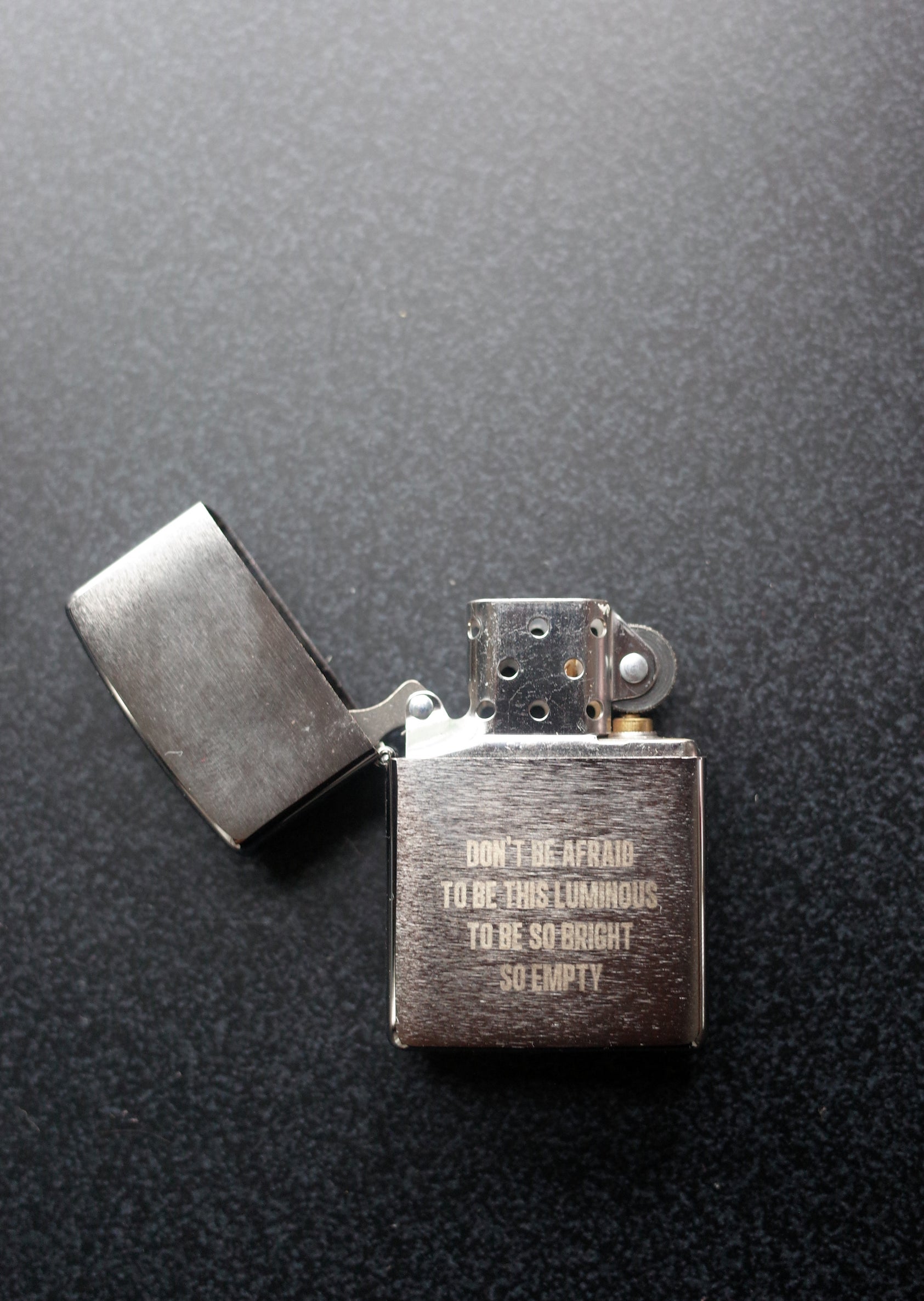 Open Zippo style lighter with the engraving "DON'T BE AFRAID TO BE THIS LUMINOUS TO BE SO BRIGHT SO EMPTY"