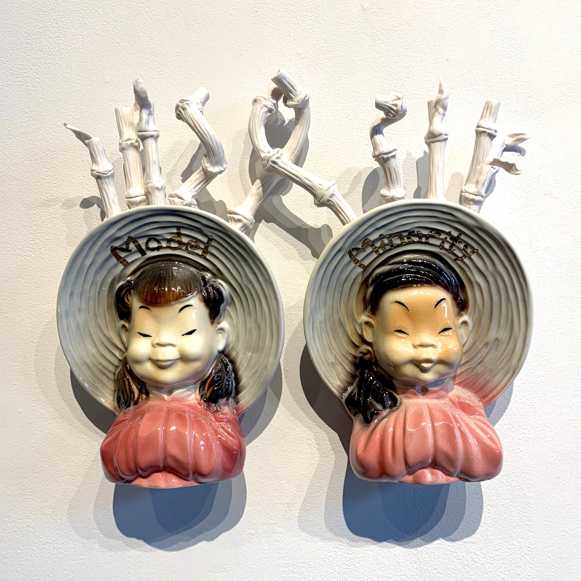 Two porcelien figures of Asian women in brimmed hats. The hats read "Model" and "Minority"