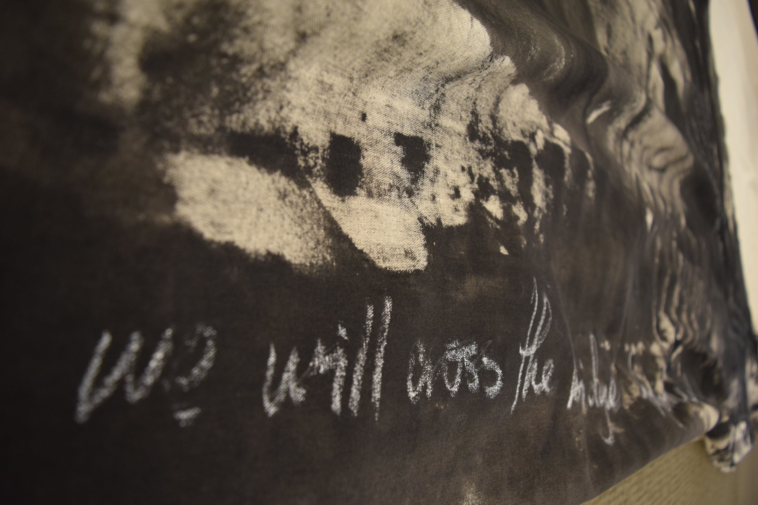 "we will cross the bridge together" written in white chalk over black paint on the canvas