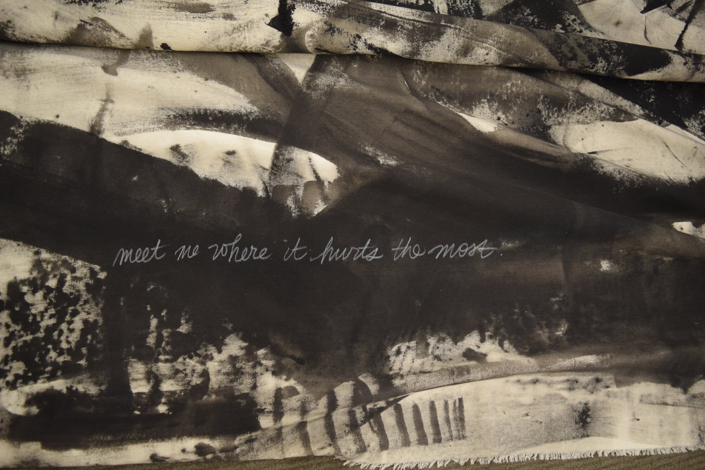 "meet me where it hurts the most" written in white chalk over black paint on the canvas