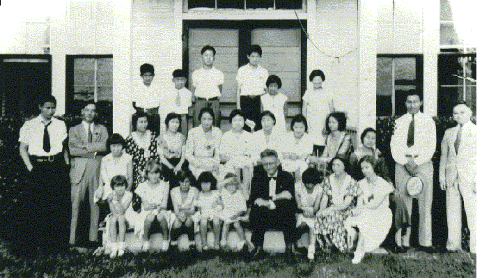 Group photo of Kishi colony residents and the minister on the porch of the Terry Methodist Chapel, circa late 1920s