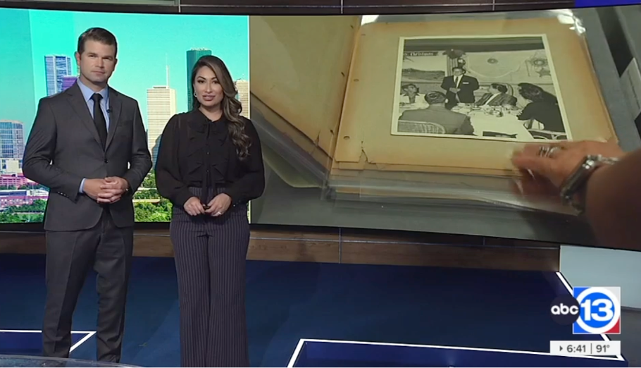 Two reporters stand in front of a screen showing a scrapbook from the Houston Asian American Archive